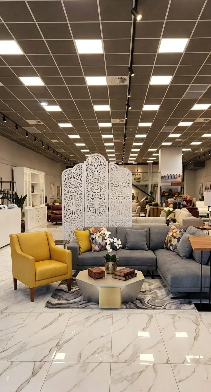 A white carved folding screen dividing a furniture showroom lounge display