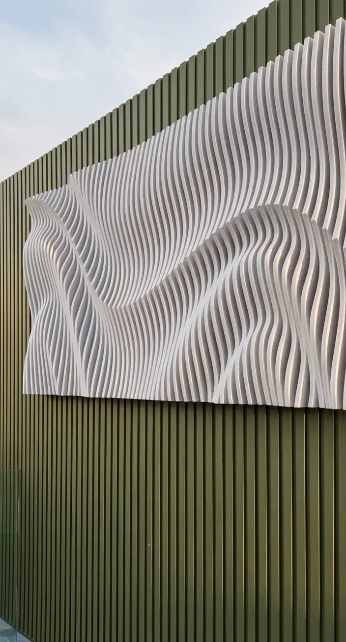 A white three dimensional wave panel mounted on green fluted exterior cladding